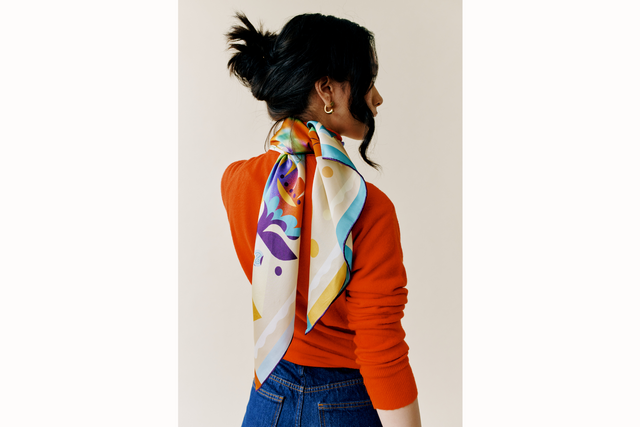 Model wears scarf draped down her back in a frenchie style with her hair up to highlight scarf.