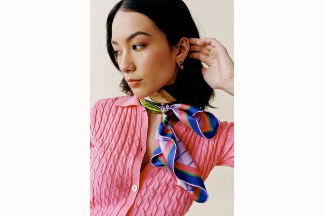 Model wears a pink cardigan and scarf tied around the neck in a frenchie style.