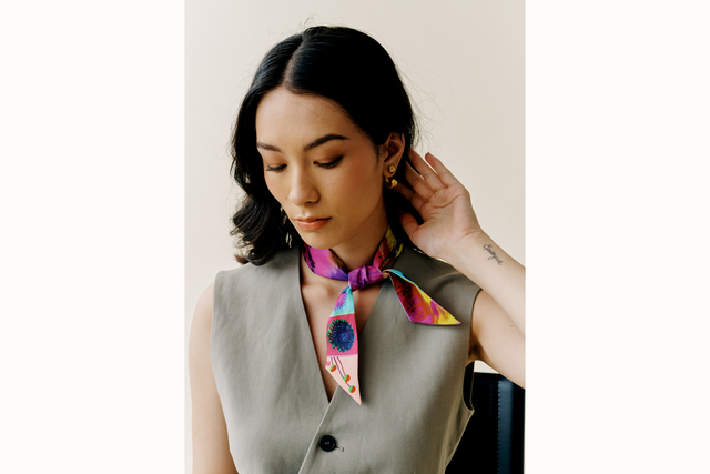 Model looks away from the camera and wears a grey vest with scarf tied around her neck