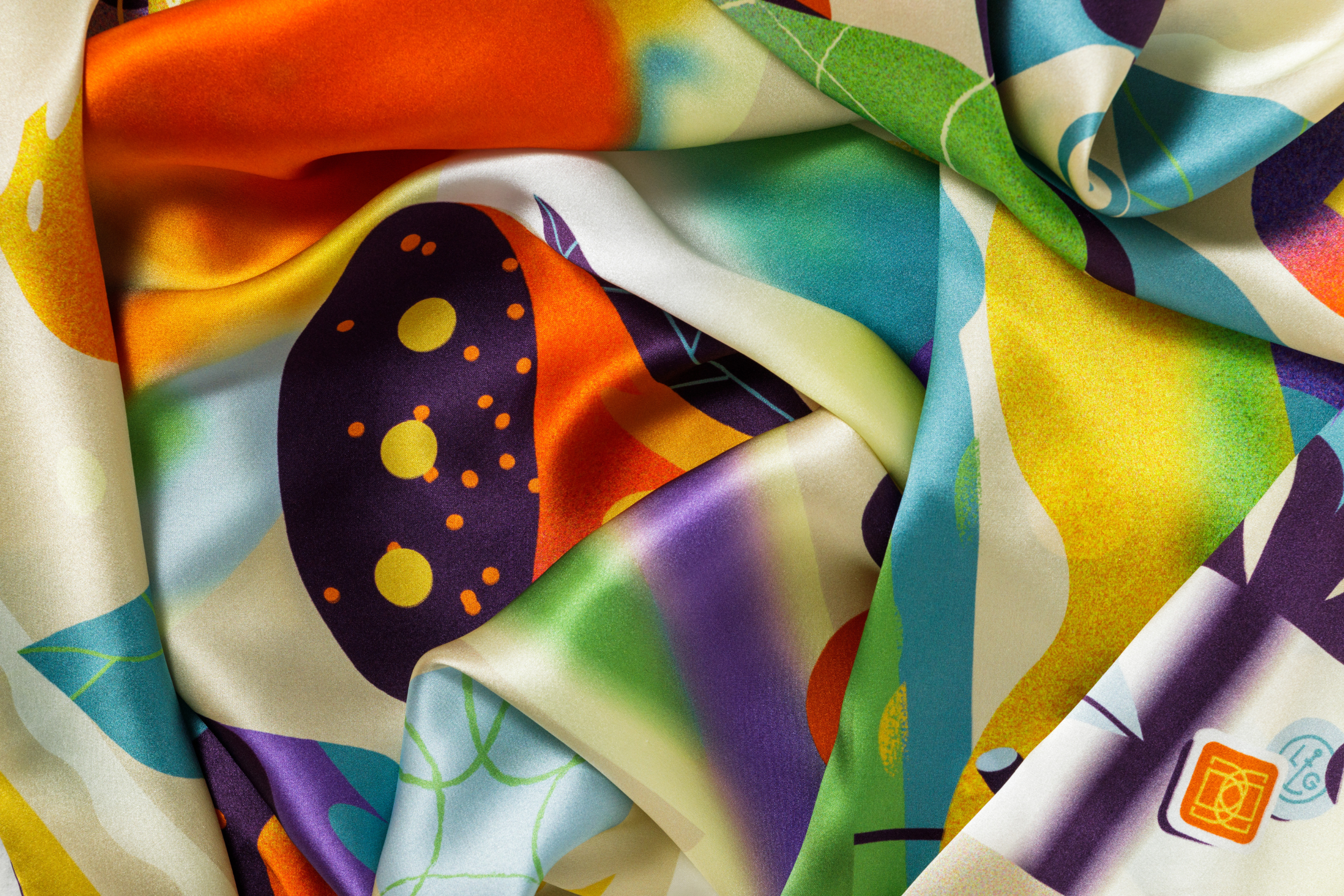 Close-up image of 100% silk square scarf featuring a collage of fruits, vegetables, and flowers in luscious shades of yellow, with pops of orange, blue, and purple throughout, illustrating the lightly ridged texture of the silk twill along with the rich color tones and luminous nature of the silk scarf.