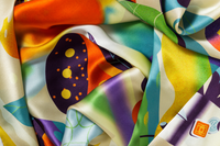 Close-up image of 100% silk square scarf featuring a collage of fruits, vegetables, and flowers in luscious shades of yellow, with pops of orange, blue, and purple throughout, illustrating the lightly ridged texture of the silk twill along with the rich color tones and luminous nature of the silk scarf.