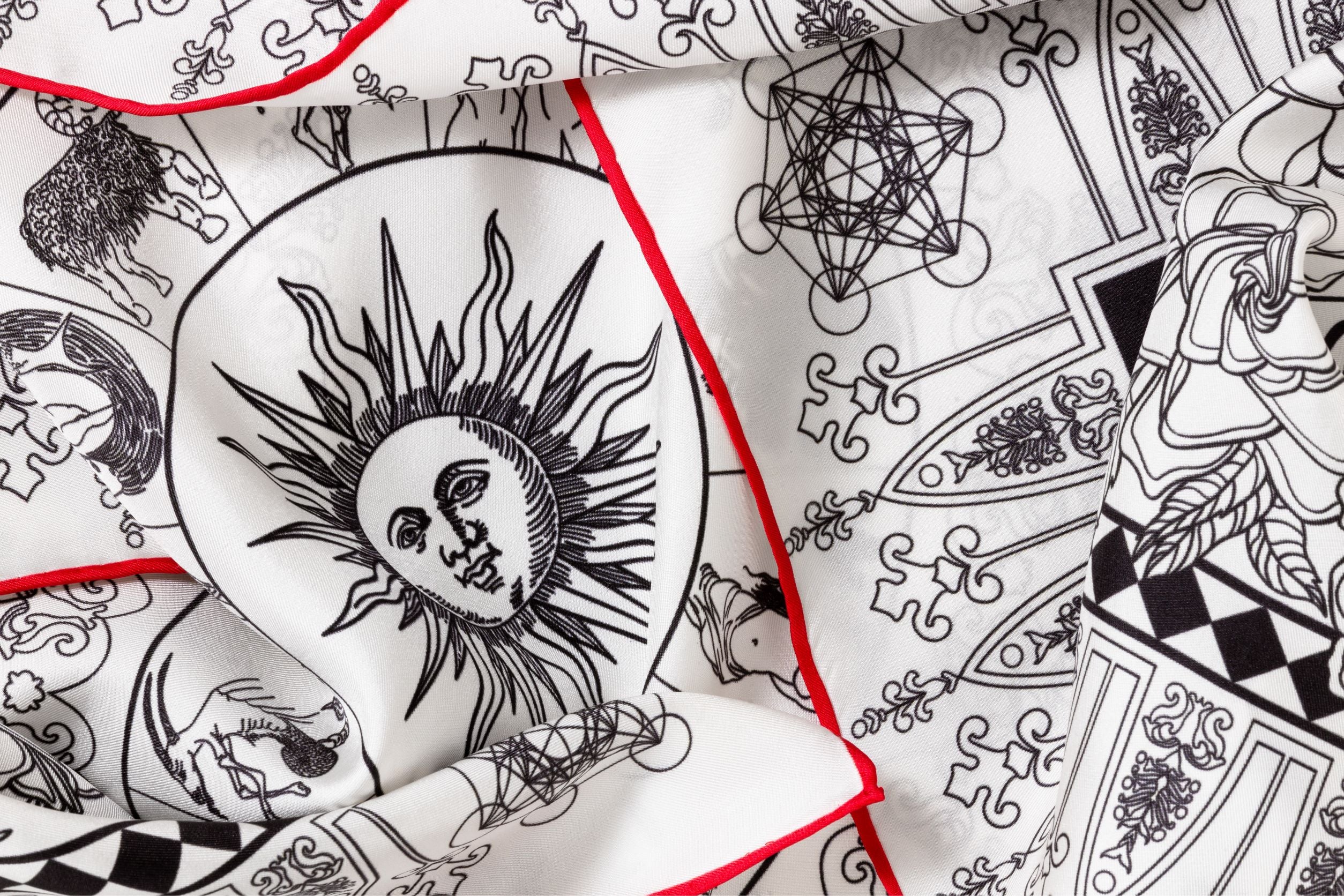 Close-up image of 100% silk square scarf featuring a black line illustration motif of zodiac, moon phases + the natural elements against a white background. Illustrates the slightly ridged texture of the silk twill along with the rich color tones and luminous nature of the silk scarf.