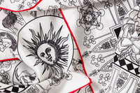Close-up image of 100% silk square scarf featuring a black line illustration motif of zodiac, moon phases + the natural elements against a white background. Illustrates the slightly ridged texture of the silk twill along with the rich color tones and luminous nature of the silk scarf.