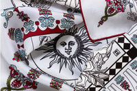 Close-up image of 100% silk square scarf featuring a black line illustration motif of zodiac, moon phases + the natural elements against a white background. Illustrates the slightly ridged texture of the silk twill along with the rich color tones and luminous nature of the silk scarf.