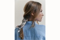 Image of a female model wearing the scarf wrapped around her and tied to be styled as a bandana along with a light blue button-down.