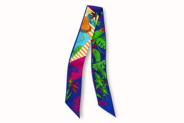 Flatlay image of 100% silk ribbon style scarf, 2” wide by 32” long. Featuring a woman swimming in a blue pool, a straw sun hat and orange and white stripes splashed across a background of green tropical leaves and pink flowers.