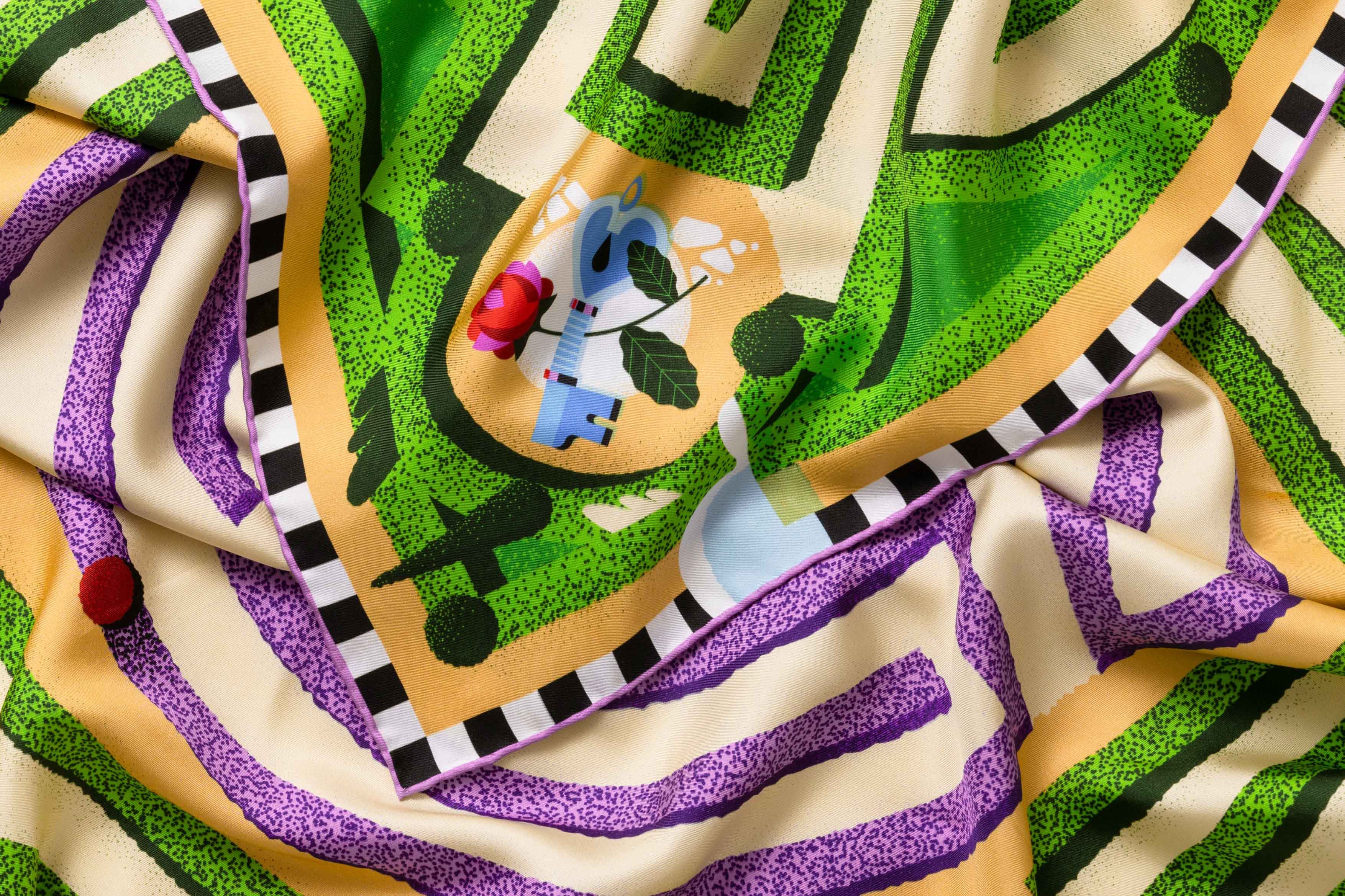 Close-up image of 100% silk square scarf featuring a motif of a garden labyrinth with green hedges and purple lavender elements on a warm cream background. Also features a blue key and floral detail in each of the four corners of the scarf as well as a black and white checker border around the edges. Illustrates the lightly ridged texture of the silk twill along with the rich color tones and luminous nature of the silk scarf.