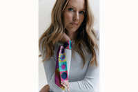 Image of a female model wearing the scarf wrapped around her wrist with the tail ends of the scarf draping down her arm. She is wearing an all white long sleeve ribbed shirt.