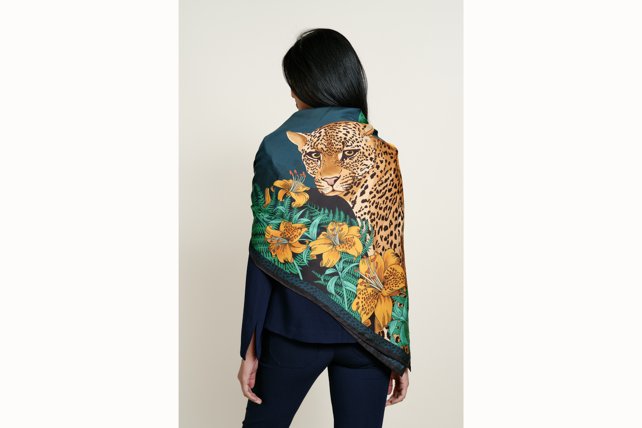 Image of a female model from behind wearing the scarf folded in half diagonally and draped across her shoulders where the leopard is predominantly featured.