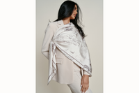 Image of a female model wearing the scarf sashed at the shoulder and tied over a neutral 2-piece blazer set near the waist of the opposite end. Model holds one hand to her slightly popped hip as she looks away from the camera.