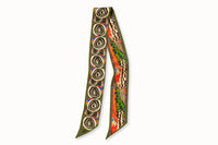 Flatlay image of 100% silk ribbon style scarf, 2” wide by 32” long. Featuring an abstract elephant motif and a pattern inspired by a traditional African painting composed of orange, army green, and hints of blue.