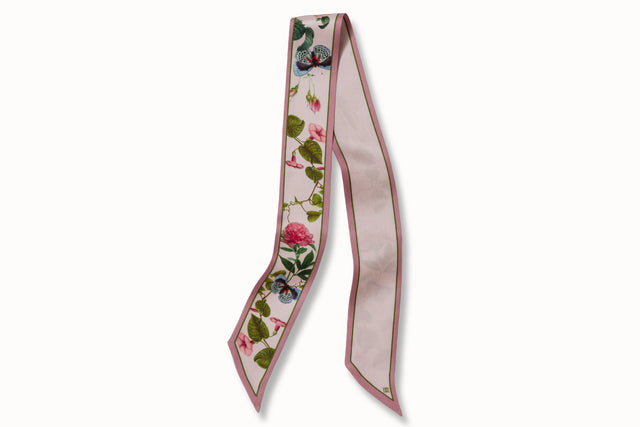 Flatlay image of 100% silk ribbon style scarf, 2” wide by 32” long. Featuring delicate peony flowers + blue butterfly illustrations coupled with a simple soft pink reverse.