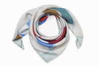 Rolled image of 100% silk square scarf featuring a grouping of squares and rectangles of various sizes on an ecru background. Colors featured include crimson, cherry, khaki, cornflower blue and teal.