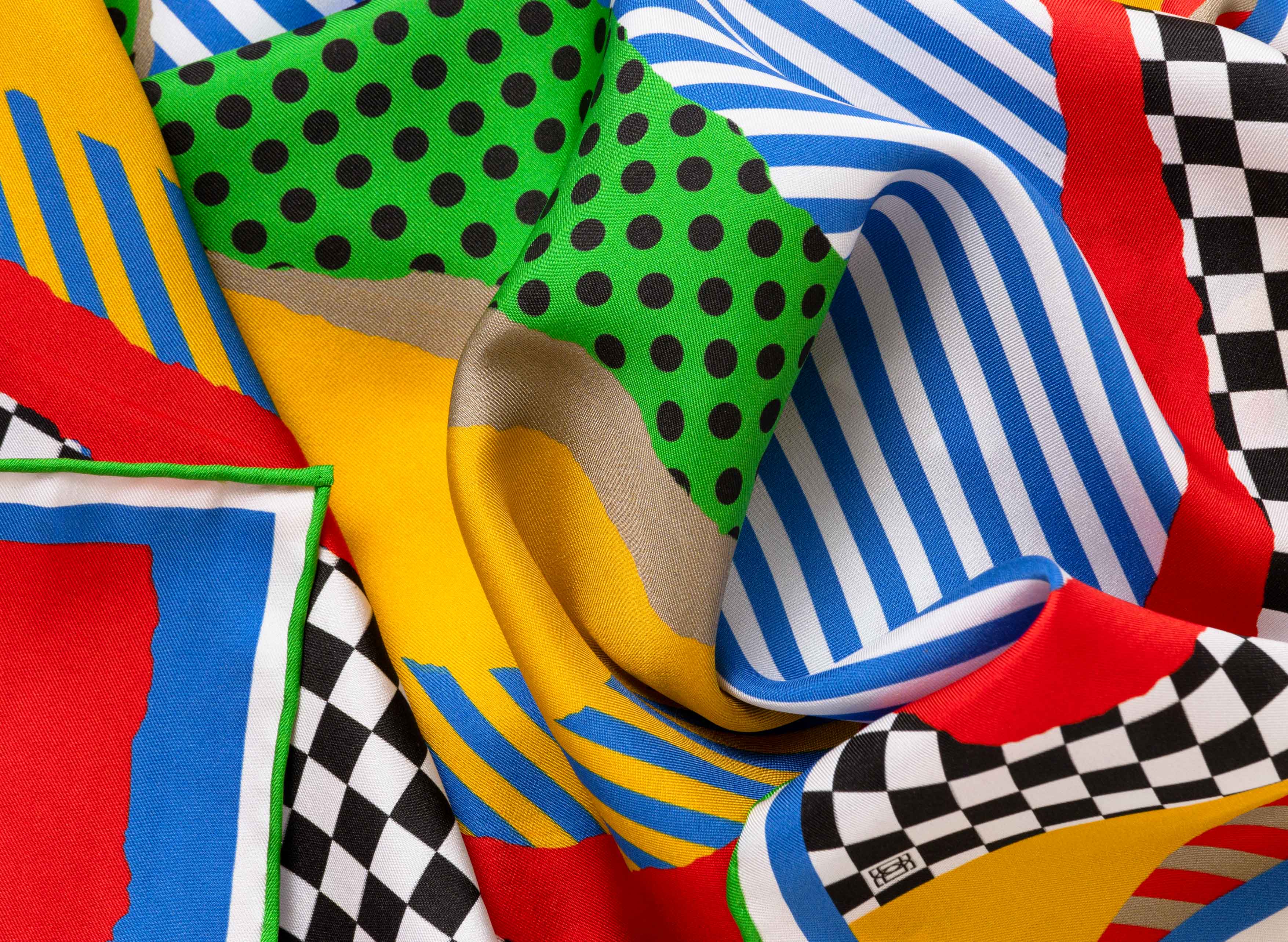 Close-up image of 100% silk square scarf featuring a high energy collage of blocks of color interrupted by lines, polka dots and checkers. Colors include black, white, stop sign red, kelly green, bright yellow and azure blue. Illustrates the lightly ridged texture of the silk twill along with the rich color tones and luminous nature of the silk scarf.