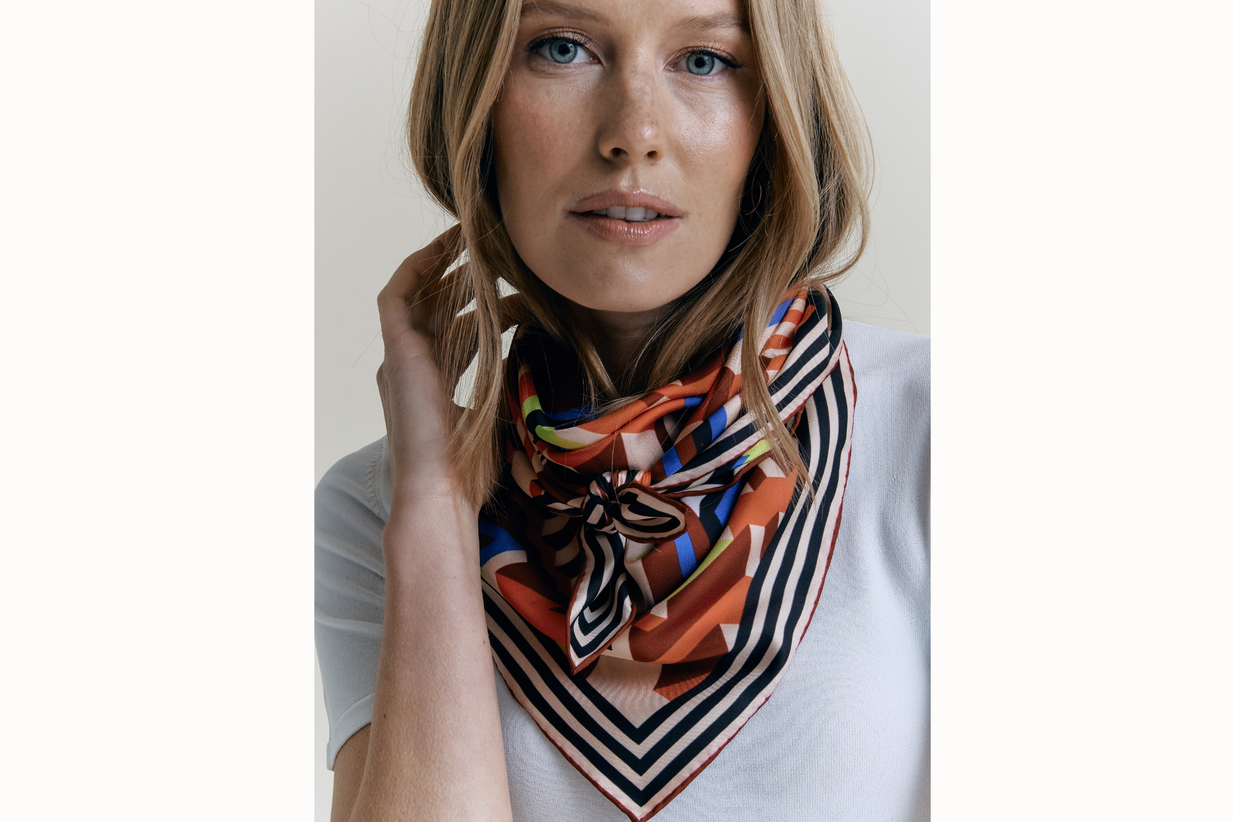 Image of female model wearing scarf folded into a triangle wrapped around and tied in the front of her neck. 