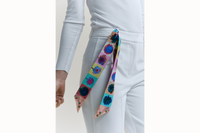 Image of a female model wearing the scarf wrapped around the belt loop of her white denim with the tail ends of the scarf draping down her leg.