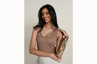 Image of female model wearing the scarf wrapped around her wrist and tied like a silk bracelet. The model is wearing a brown tank and cream pants.