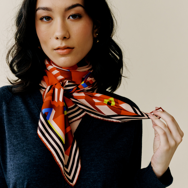 Model wears scarf styled in a cowgirl knot and holds an end of the scarf