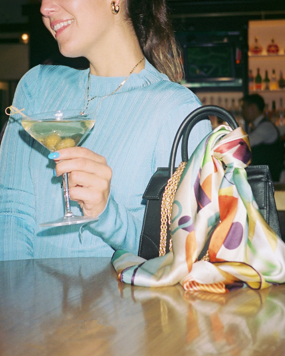woman holds martini next to her bag with a scarf styled on it