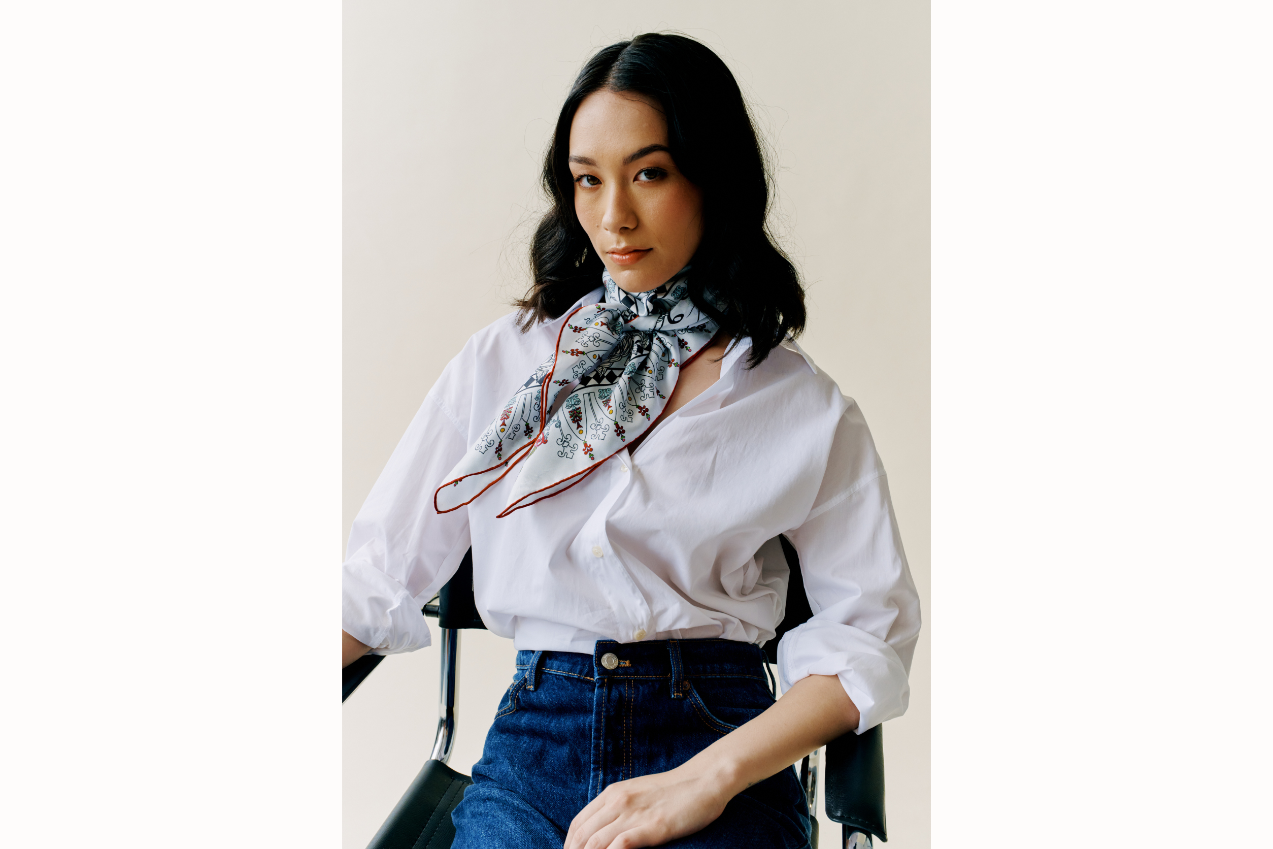 female model wears denim and white button down with scarf tied around her neck. Tails of scarf blow to the left