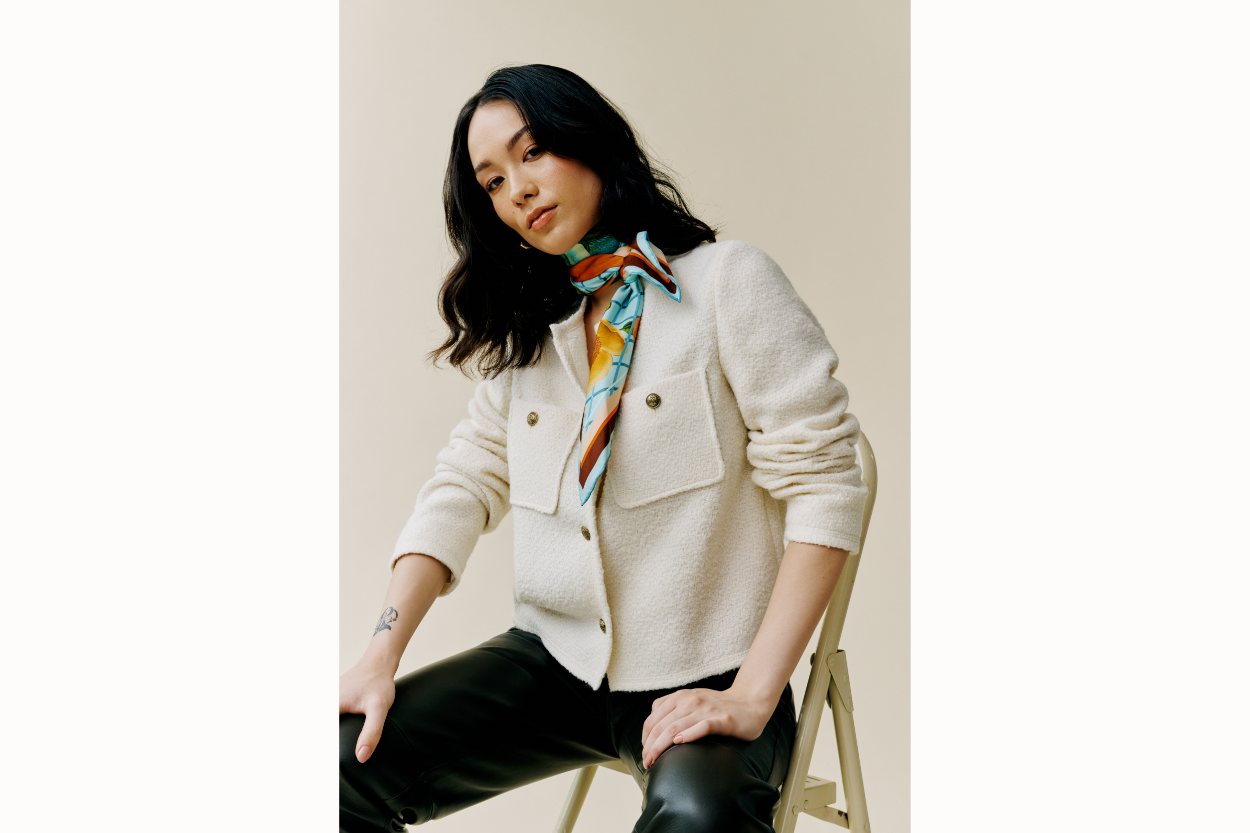 female model sits on a step ladder and wears a textured cardigan, leather pant and scarf styled around the neck