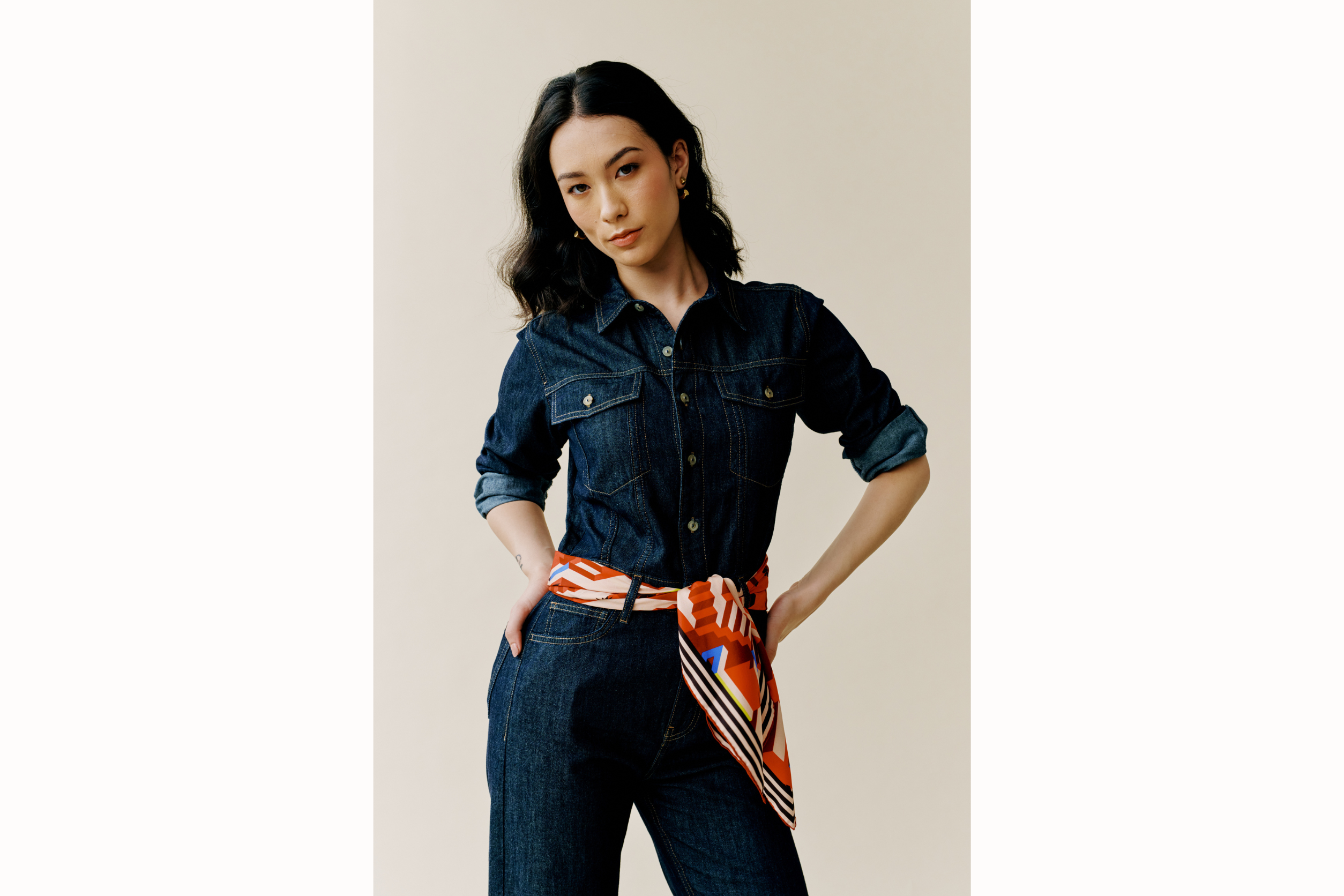 Model wears denim jumpsuit and scarf styled as a belt. 