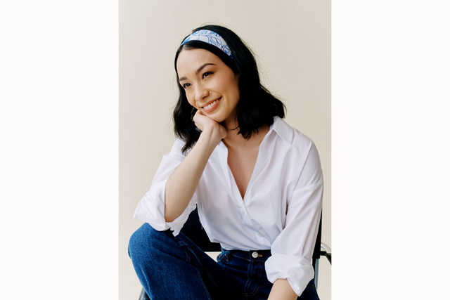 Model smiles posed with her hand resting on chin and wearing a twiggy scarf styled as a headband