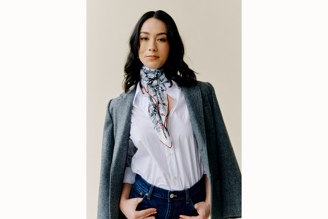 female model wears a charcoal blazer, white button down, and scarf tied around neck with tails draped down her chest 