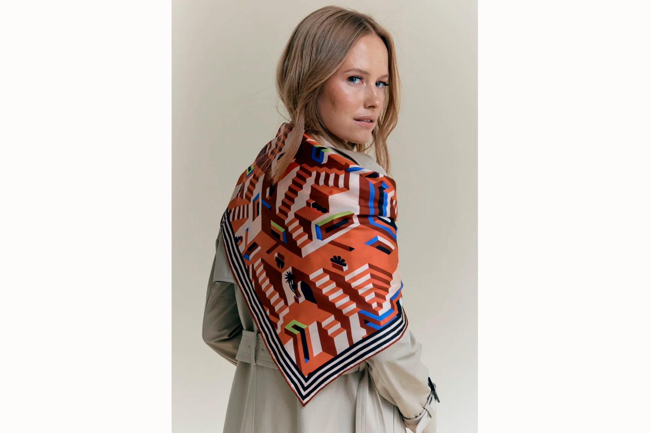  Image of the back female model looking off to the right while wearing the scarf draped over the shoulder of a neutral trench coat.  