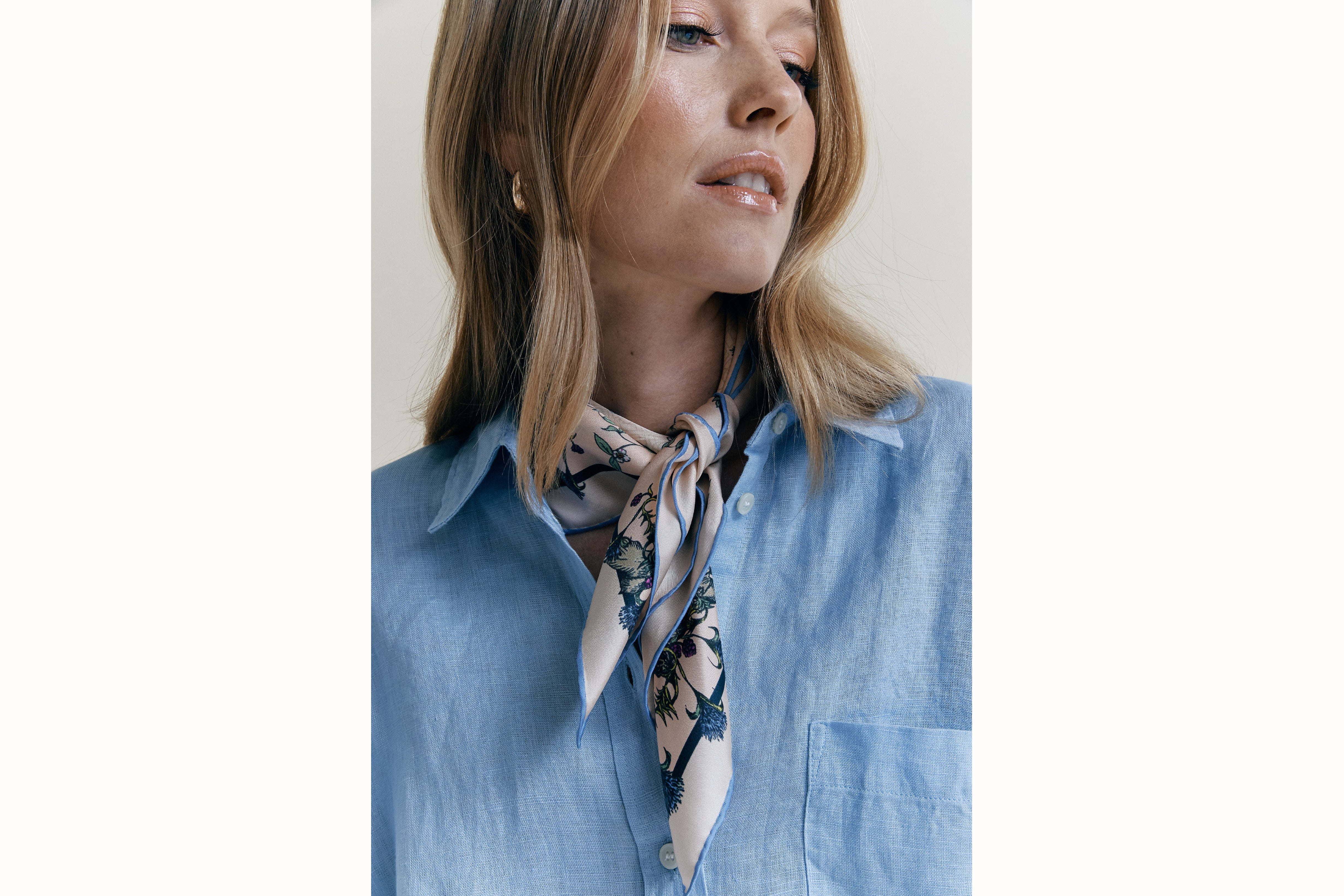  Image of a female model wearing the scarf wrapped around her and tied to be styled as a bandana along with a light blue button-down. 