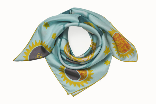 Rolled image of 100% silk square scarf featuring a motif of featuring a motif of stars, the sun and the moon phases positioned around planet Earth. Details in shades of rich turquoise, marine blue, white, chartreuse and maize on a light turquoise background.