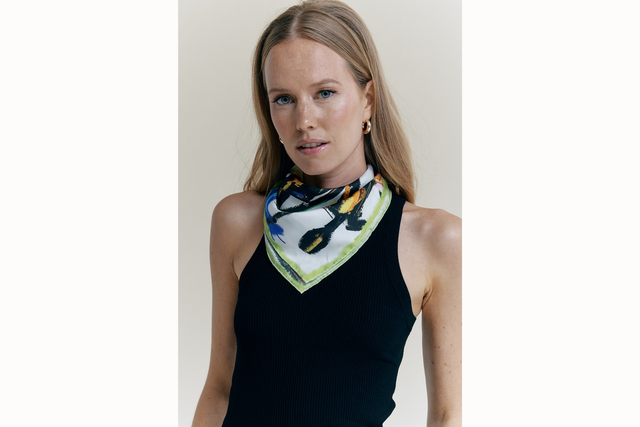 Image of female model wearing the scarf tied as a bandana around her neck. She is also wearing a black tank top. 