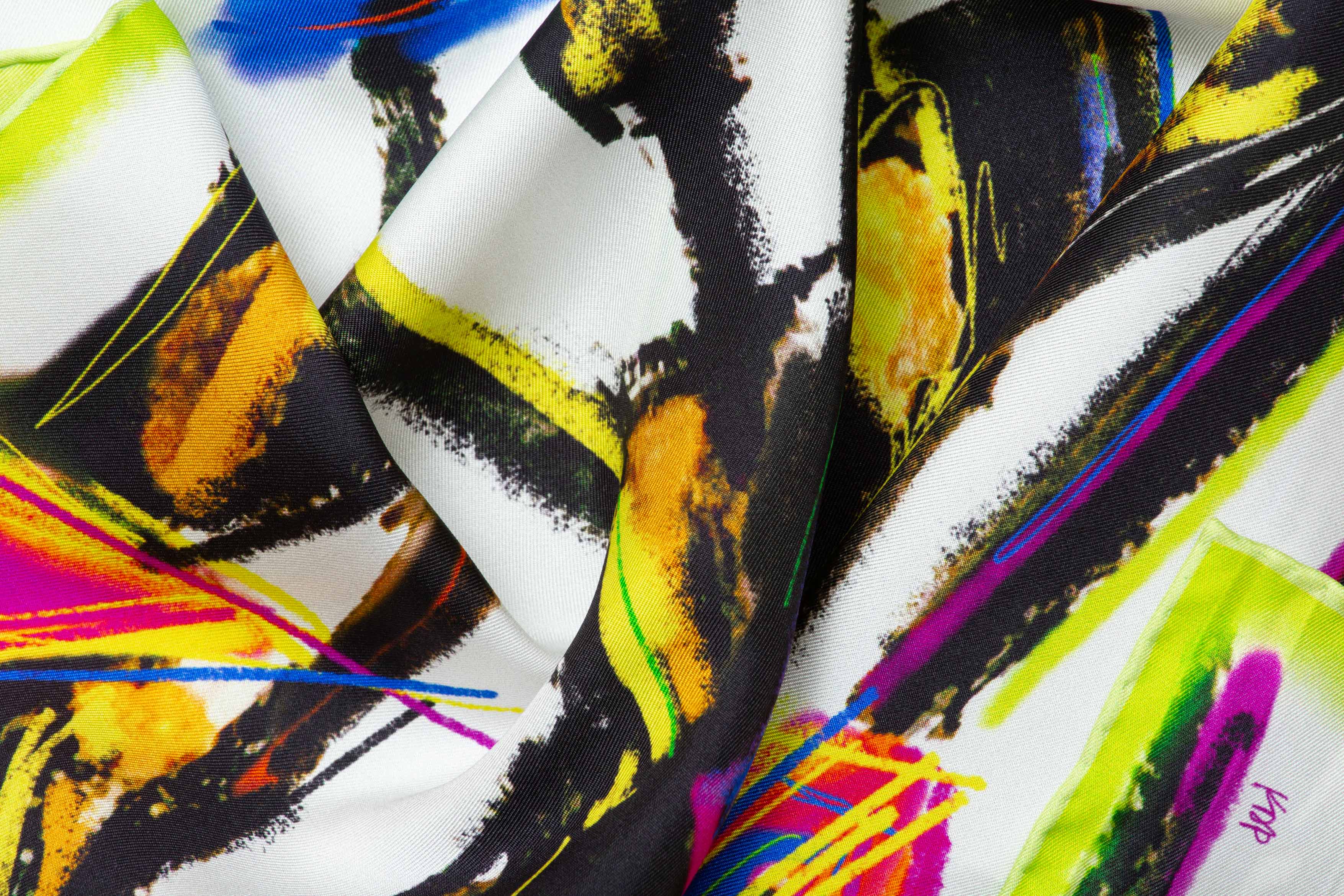 Close-up image of 100% silk square scarf featuring a motif of five black female stick figures all wearing scarves styled in different ways. The scarves are in various shades of neon pink, green, yellow and blue splashed across a white background. Illustrates the lightly ridged texture of the silk twill along with the rich color tones and luminous nature of the silk scarf.