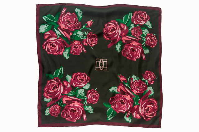 Flatlay image of 100% silk square scarf featuring a motif of large-scale roses and leaves in shades of rich red and green on a background of deep green, with a dark burgundy border around the edges.