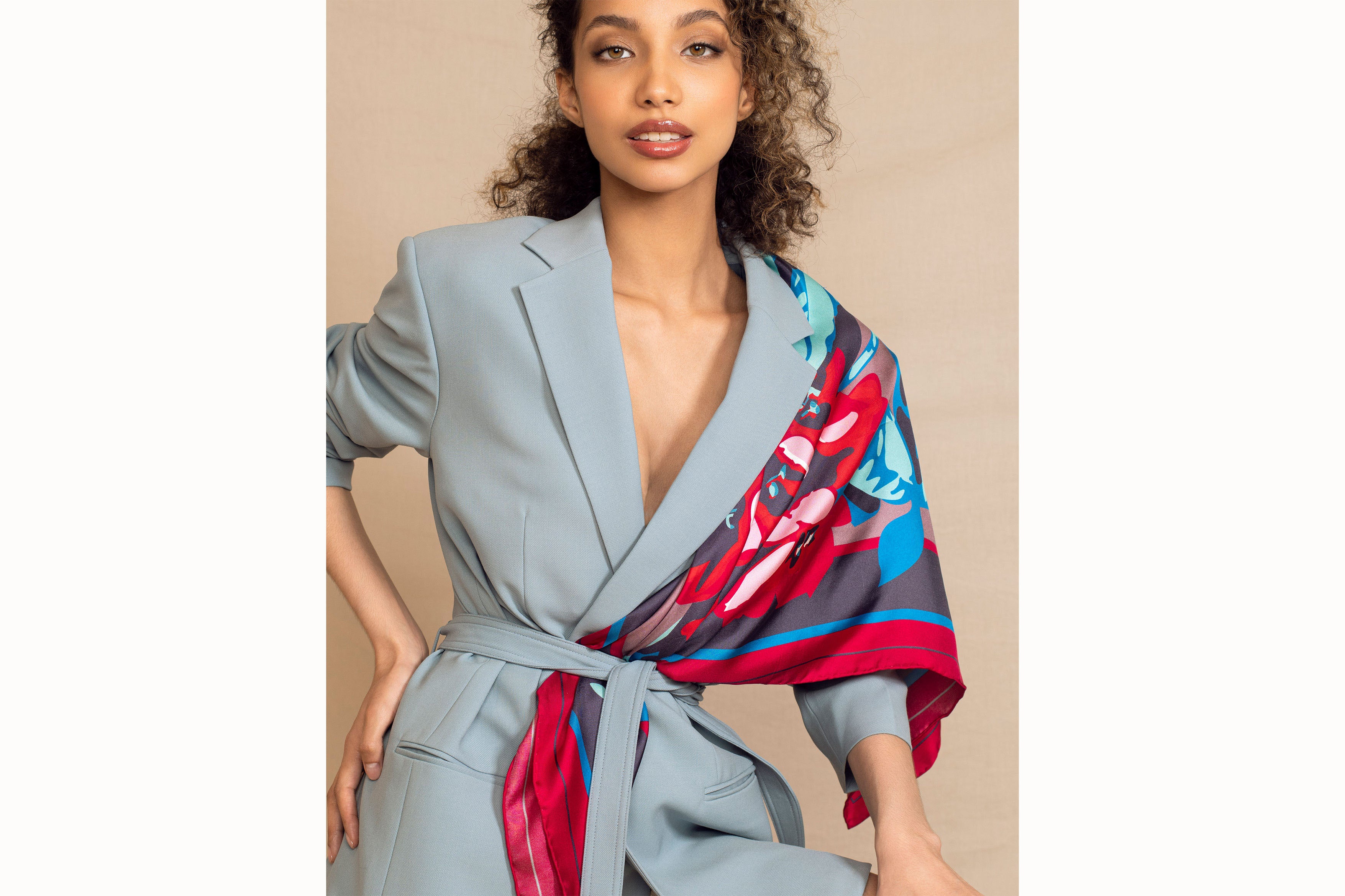 Image of female model with hands on hips while wearing the scarf folded in a triangle and over the right shoulder and tucked into the sash of a blue blazer.