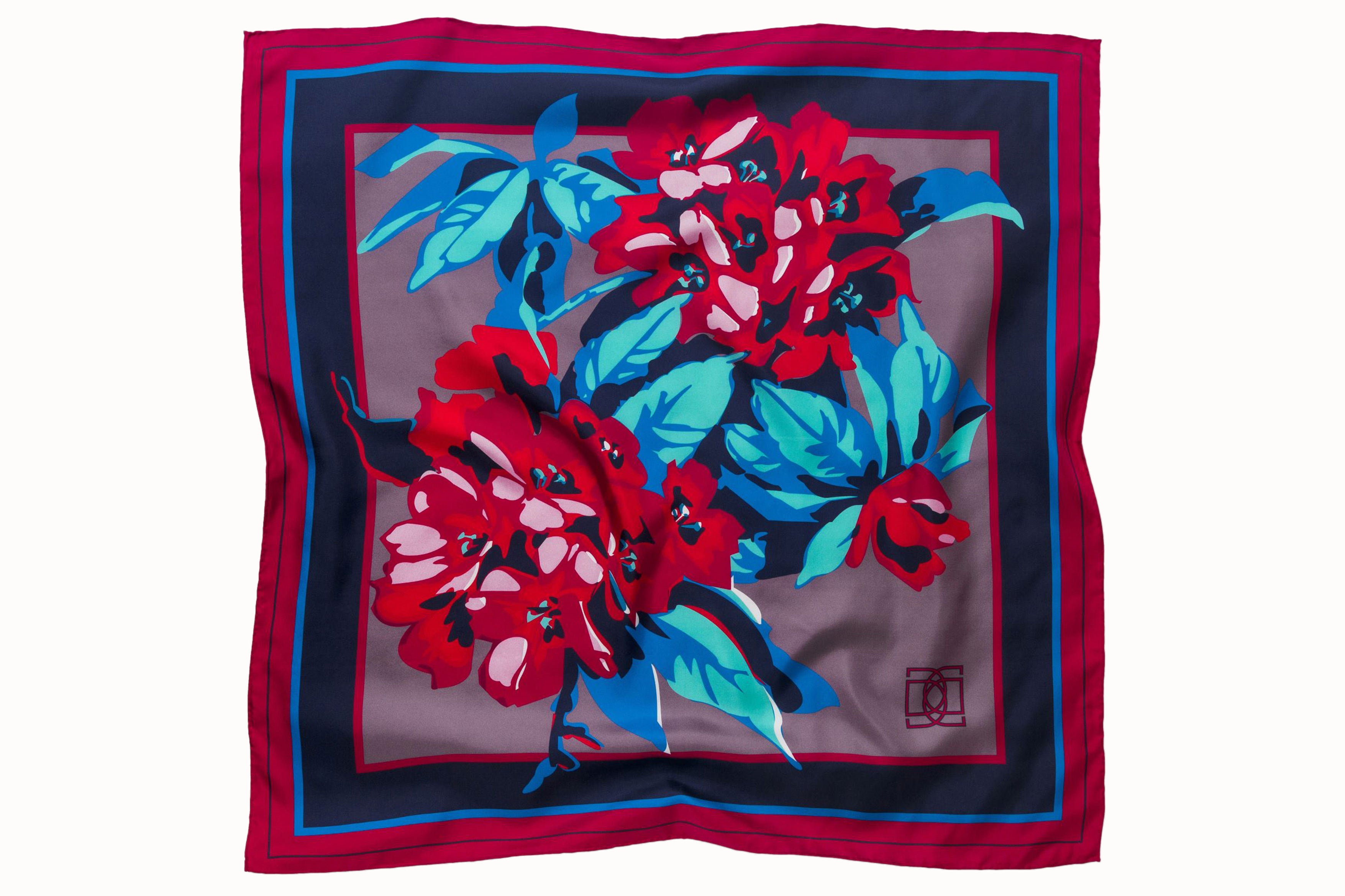 Flatlay image of 100% silk square scarf featuring a motif of large-scale florals and leaves in shades of rich red, magenta, berry and marine blues on a background of smoky lilac, with a dark blue and magenta border around the edges.