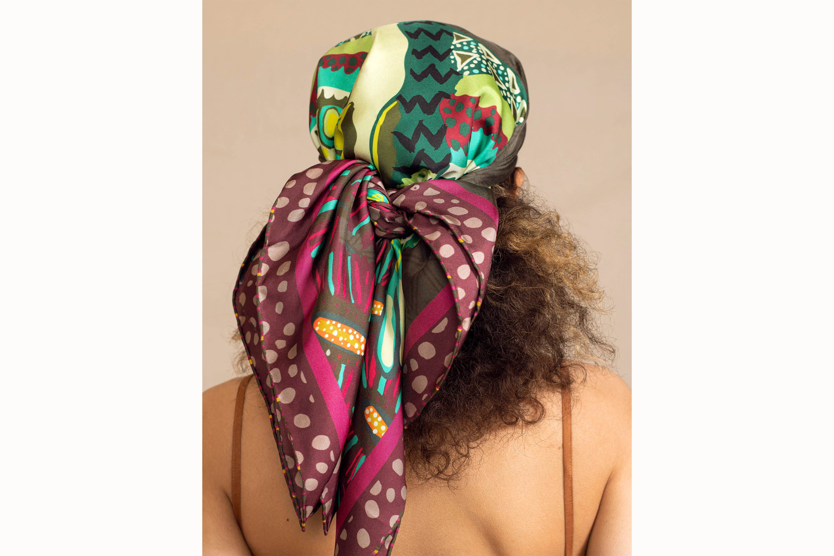 Image of female model with curly brown hair from the back, wearing the scarf tied around her head like a bandanna.