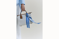 Image of the scarf wrapped around the handle of a white bag with the tail ends of the scarf draping down the back.