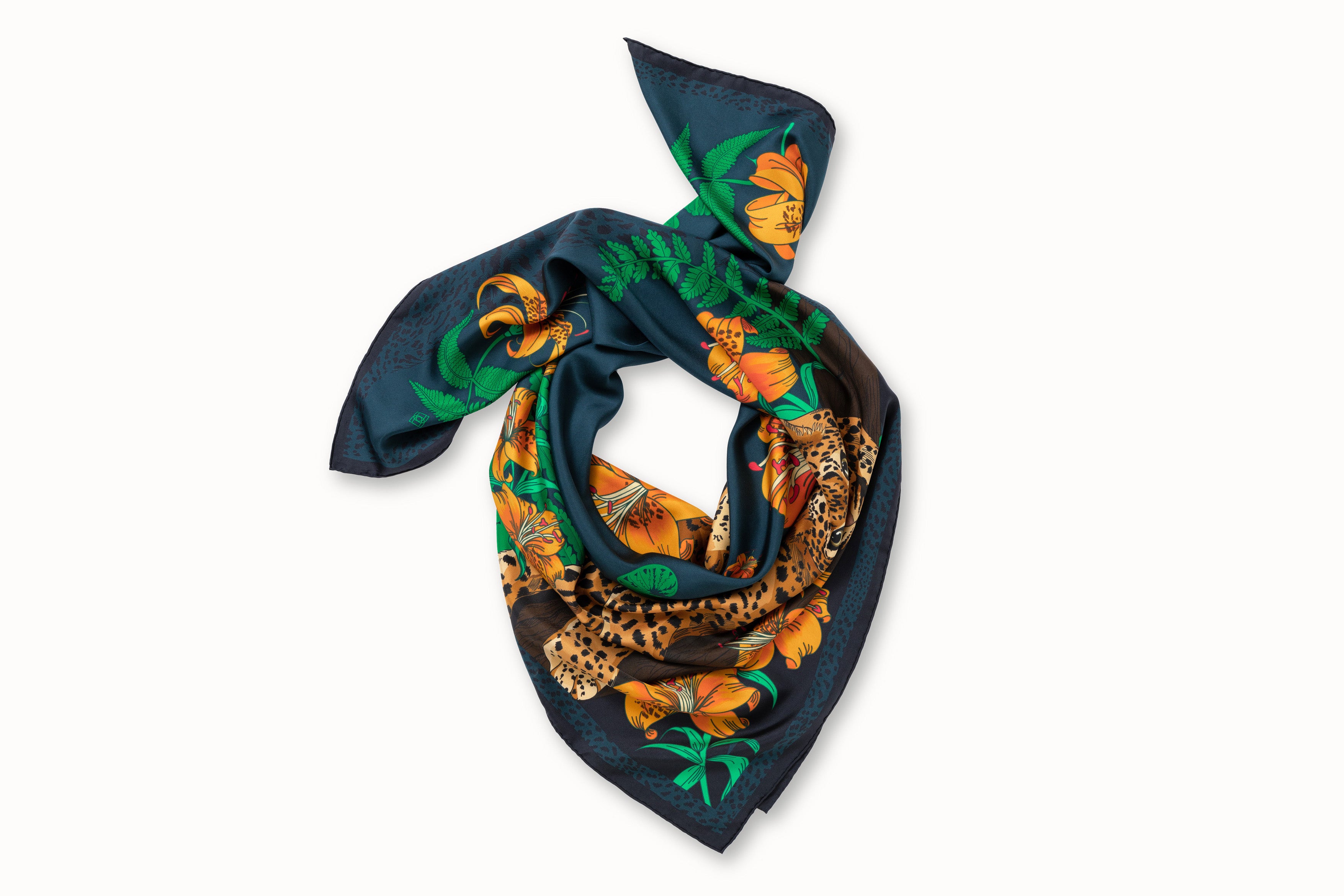 Rolled image of 100% silk square scarf featuring a motif of two leopards lounging in a jungle scene surrounded by lush greenery and tiger lily florals on a marine blue background.