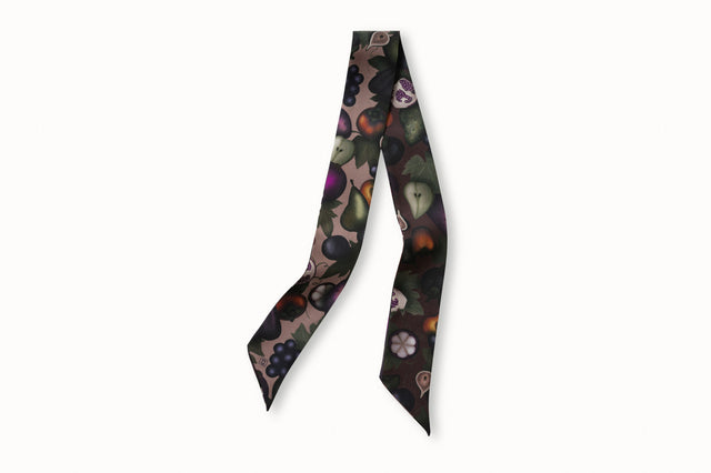 Flatlay image of 100% silk ribbon style scarf, 2” wide by 32” long. Featuring a illustrations of rich, ripe fruits such as grapes, pears and persimmons in deep fall color tones such as plums, forest green, camel and burgundy. The opposite side of the scarf features the same fruit motif on a rich blush colored background.
