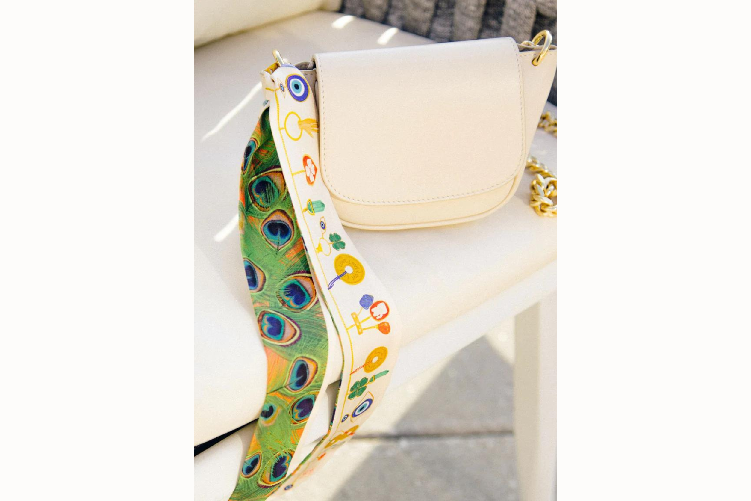 Image of scarf tied around the corner of a small white purse which rests on a chair. 