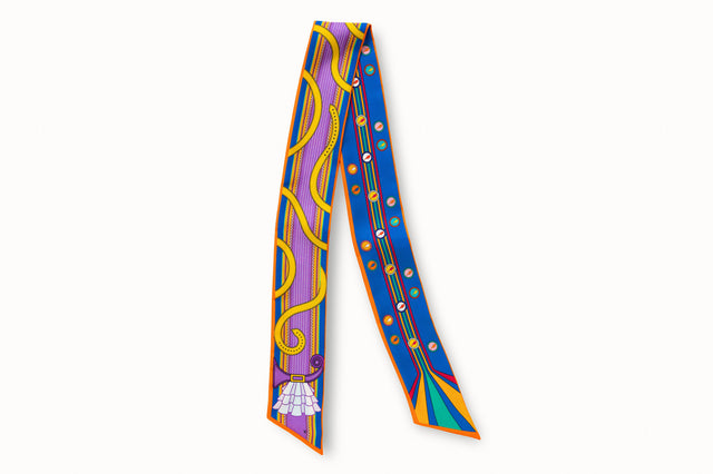 Flatlay image of 100% silk ribbon style scarf, 2” wide by 32” long. Featuring an illustration of a purple guitar neck splashed with yellow buckles and white ruffles at one end. Includes an orange border. The opposite side features lighting bolts in a variety of bright colors on a medium royal blue background.