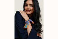 mage of female model wearing the scarf wrapped around her wrist and tied like a silk bracelet. Model is wearing a navy coord ensemble with her black hair brushed to her right side.