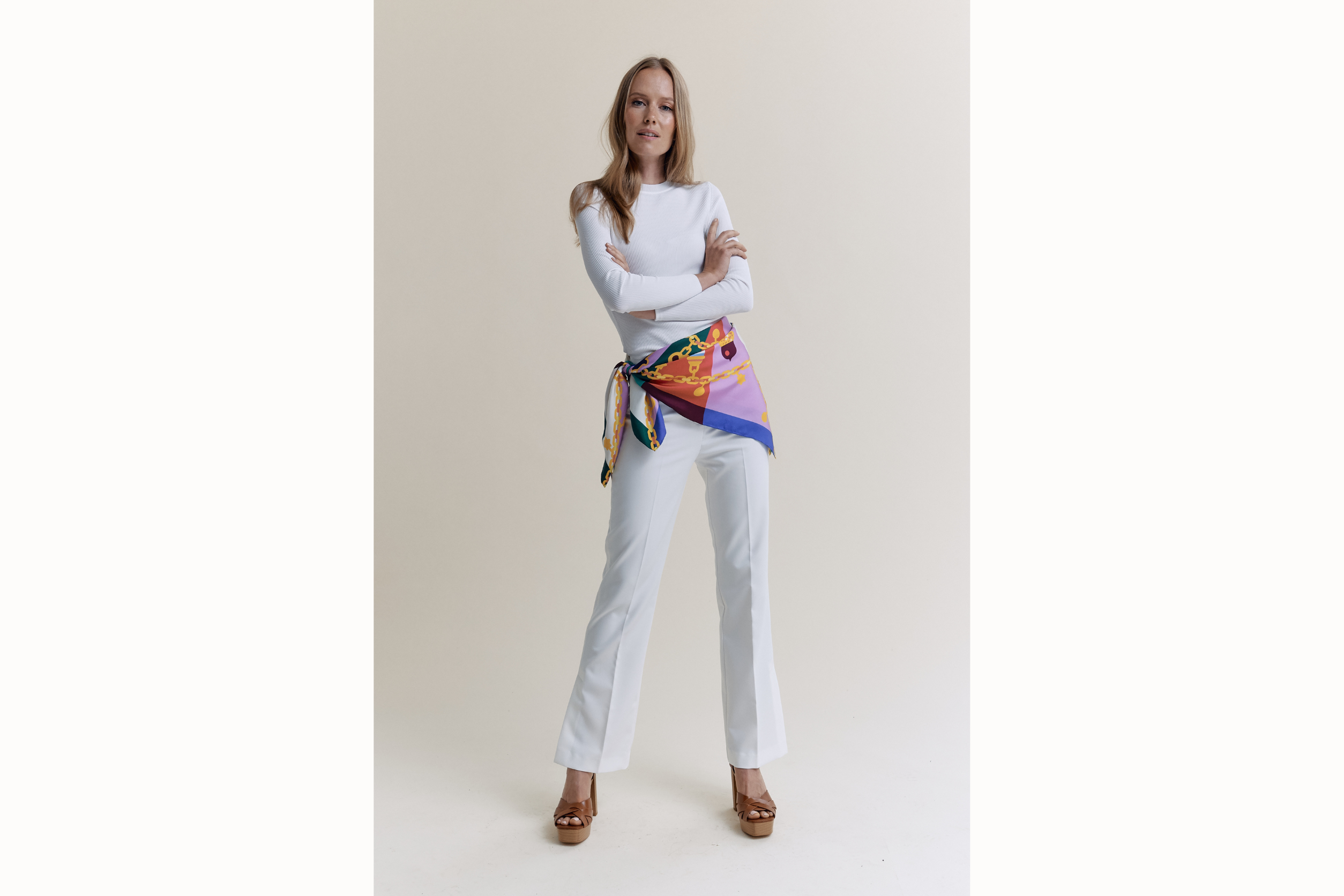 Image of a female model wearing the scarf folded in half and tied as a belt against an all white ensemble. 
