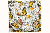 Flatlay image of 100% silk square scarf featuring a motif of large-scale illustrated monarch wings and milkweed plants on a white background with imperfectly shaped black polka dots. Thin black border on the scarf.