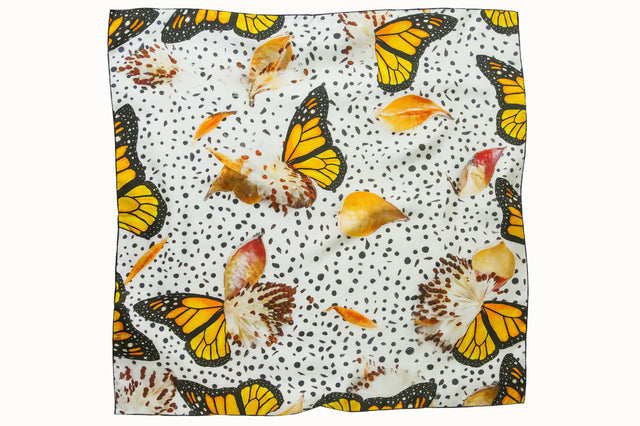 Flatlay image of 100% silk square scarf featuring a motif of large-scale illustrated monarch wings and milkweed plants on a white background with imperfectly shaped black polka dots. Thin black border on the scarf.