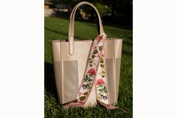Photo of scarf tied around the handle of a taupe leather tote that sits in the grass