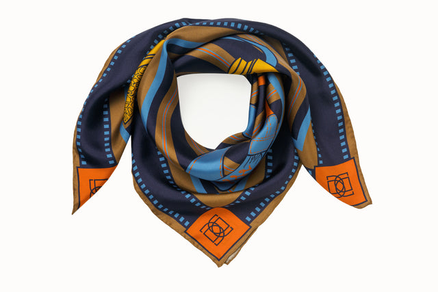 Rolled image of 100% silk square scarf featuring a motif of two large-scale illustrated film cameras and their straps splashed on top of a multi-color striped background. Blue film-inspired border around scarf. Design features colors such as orange, navy, camel, maize and a touch of aqua.