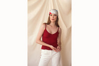 Image of female model wearing the scarf tied as a headscarf with the tails of the scarf draping over the back of her shoulders. Model also wearing a crimson tank top and white trousers.