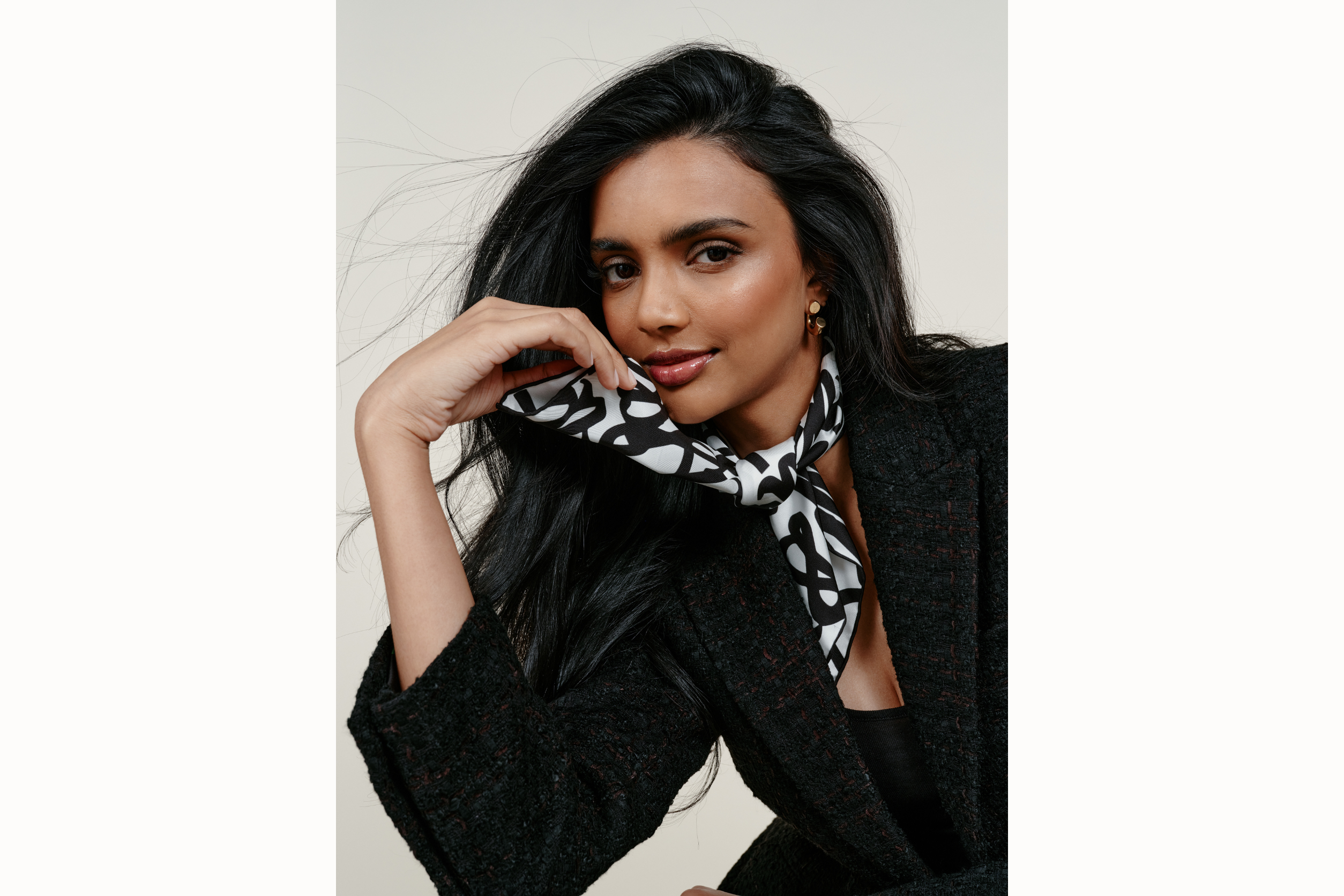 Image of female model wearing scarf rolled and tied around her neck in a "frenchie" style. She holds one of the ends in her hand as she looks into the camera.